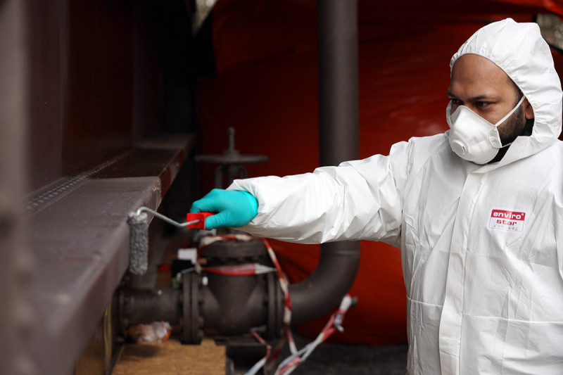 Eine graue Deckfarbe wird auf die Außenhülle des Gasometers gerollt.