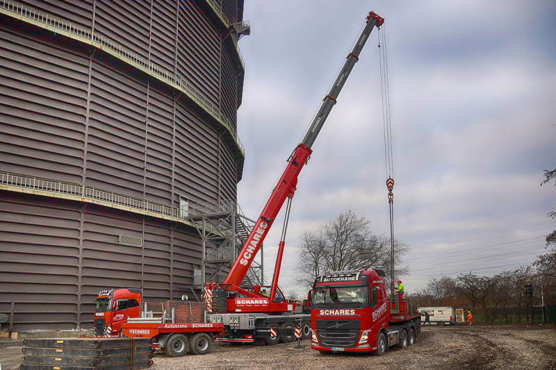 Ein roter Autokran entlädt Bauteile von einem weiteren LKW.