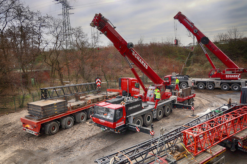 Zwei Autokräne entladen auf der Rückseite des Gasometers einen LKW.