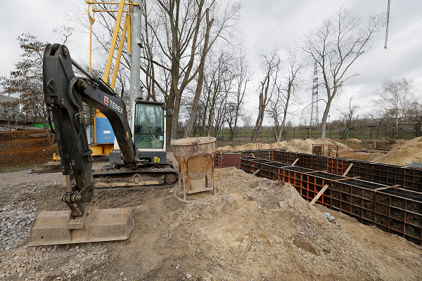 Ein Bagger vor den eingeschalten Streifenfundamenten der neuen Lagerhalle