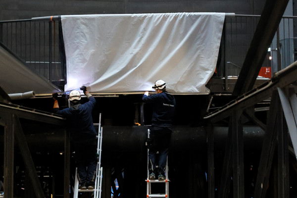 Zwei Arbeiter auf Leitern bereiten eine Stoffbahn vor.