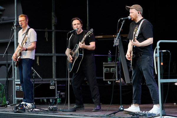 Am Mikro stehen drei Band-Mitglieder mit Gitarren der Gruppe Mottek