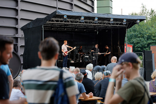 Band spielt auf dem Außengelände des Gasometers – umgeben von Besuchern - auf einer kleinen Bühne.