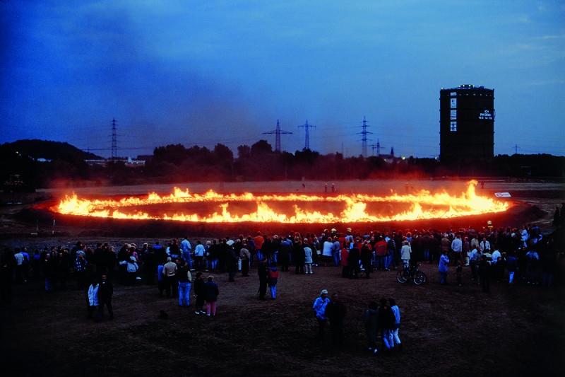 Zuschauermenge vor einem Ring aus Feuer mit dem Gasometer im Hintergrund