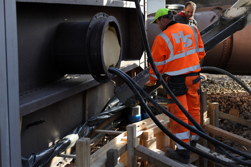 Arbeiter füllen Beton aus einem Betonmischer in eine Verschalung am Fundament des Gasometers.