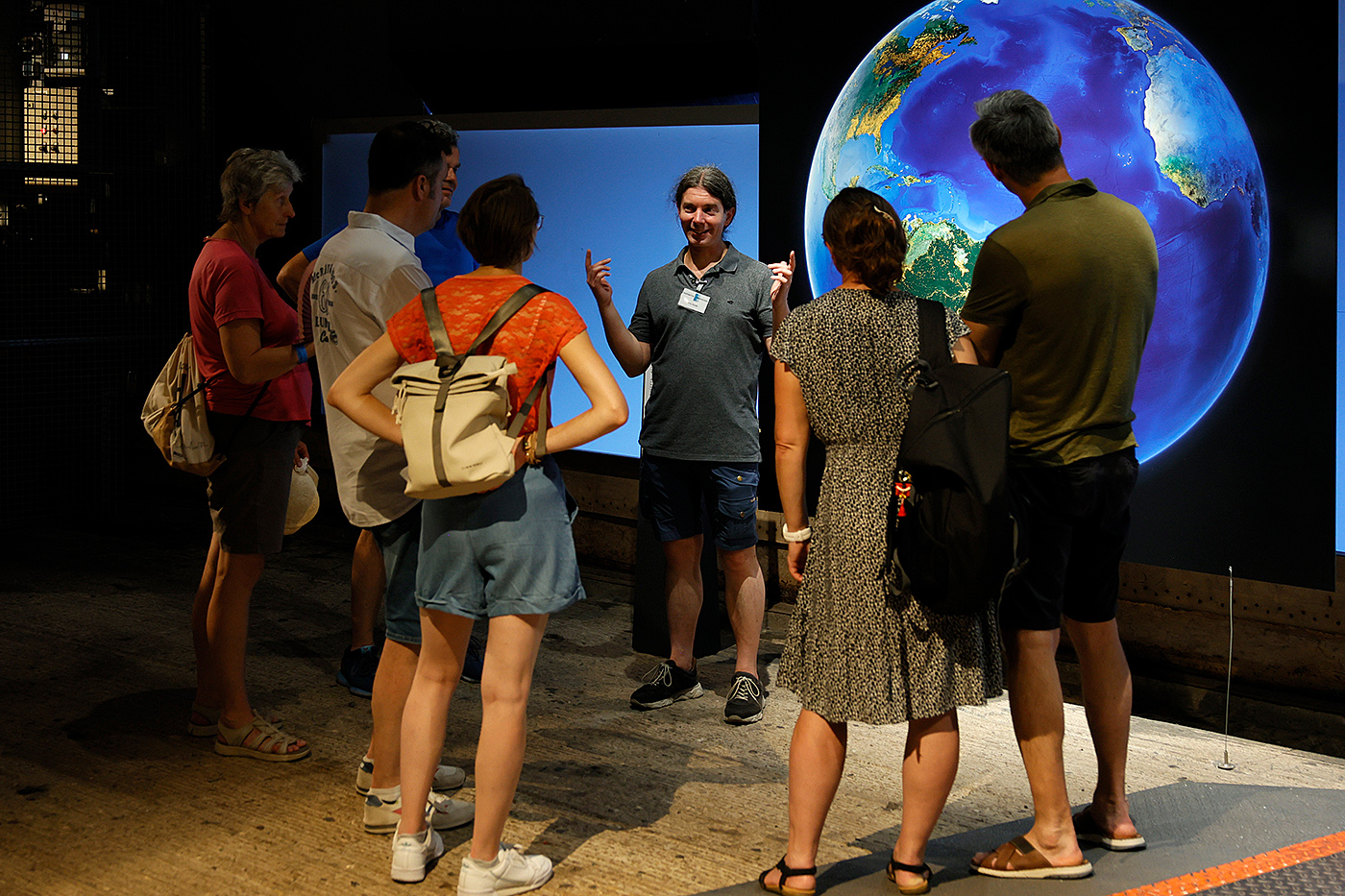 Eine Besuchergruppe nimmt an einer Führung durch die Ausstellung „Mythos Wald“ im Gasometer Oberhausen teil. Ein Gästeführer erklärt vor einer großformatigen Darstellung der Erde die Zusammenhänge zwischen Wald, Klima und unserem Planeten.