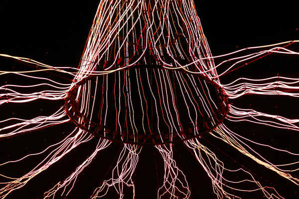 Illuminierte Lichtinstallation „Der Baum“ im Gasometer Oberhausen mit rot leuchtendem Stamm und Wurzeln in dunkler Atmosphäre. Mittig unter dem Stamm inmitten der Wurzel steht ein kleines Kind.